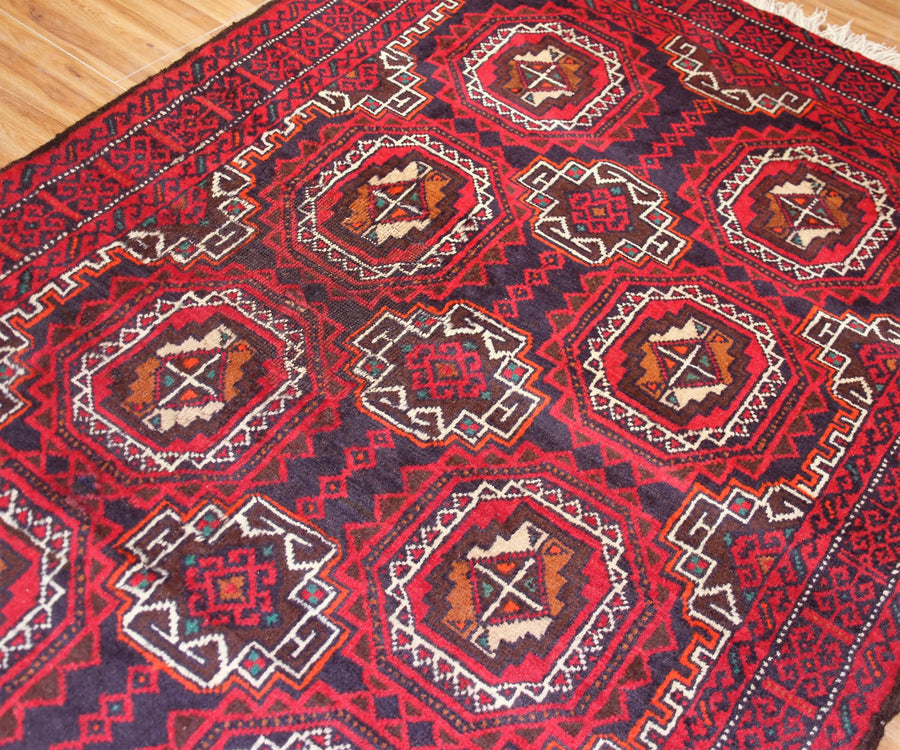 Detailed view of Baluchi Persian rug field with traditional tribal motifs in red, navy and ivory
