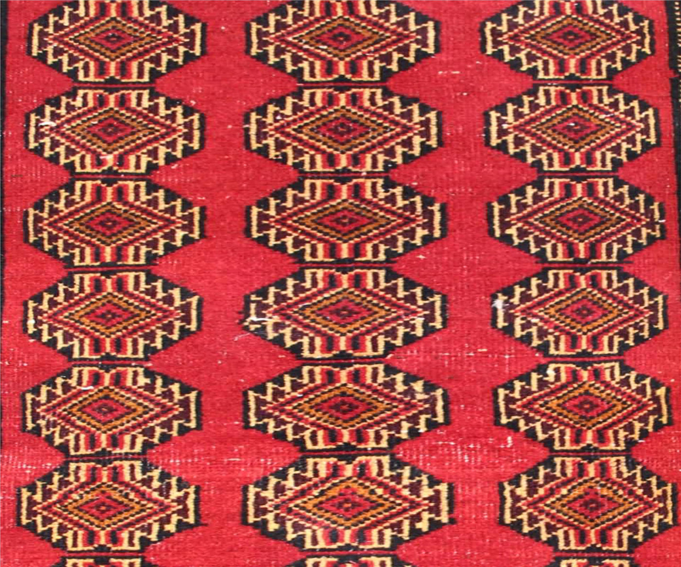 Detailed view of Turkmen runner field with diamond shaped tribal medallions in red, gold and black tones
