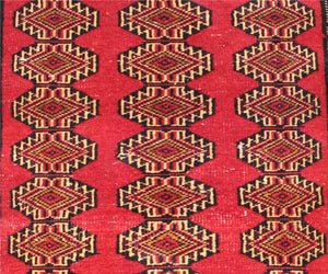 Detailed view of Turkmen runner field with diamond shaped tribal medallions in red, gold and black tones
