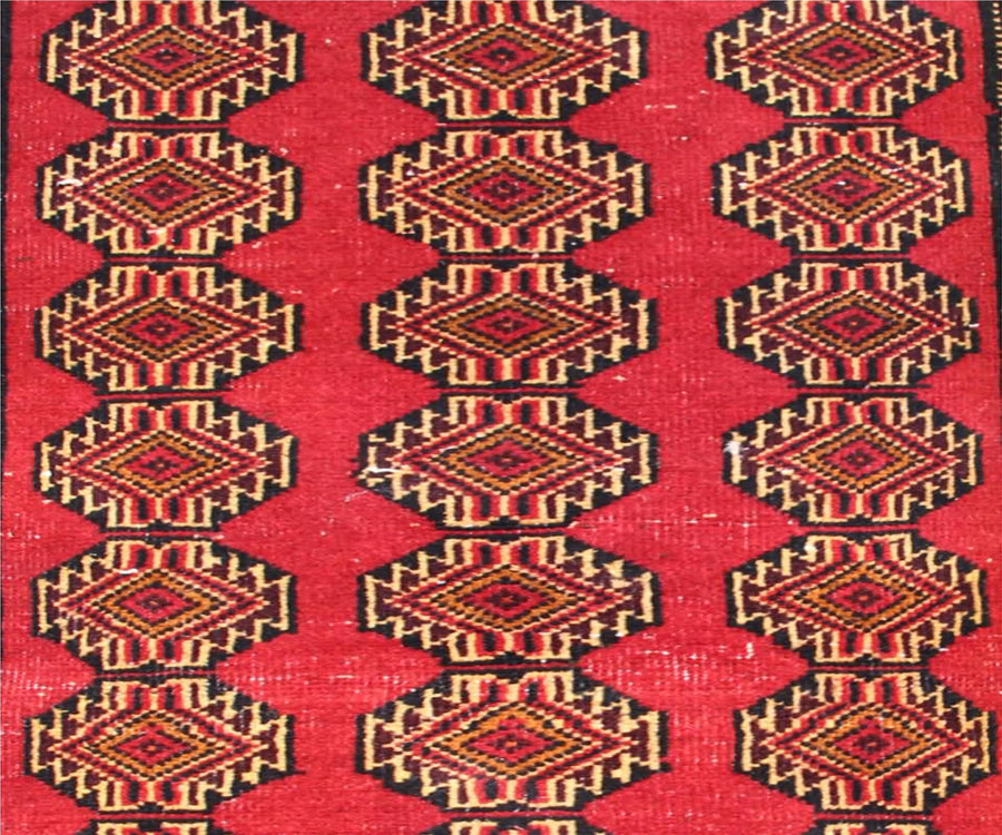 Detailed view of Turkmen runner field with diamond shaped tribal medallions in red, gold and black tones
