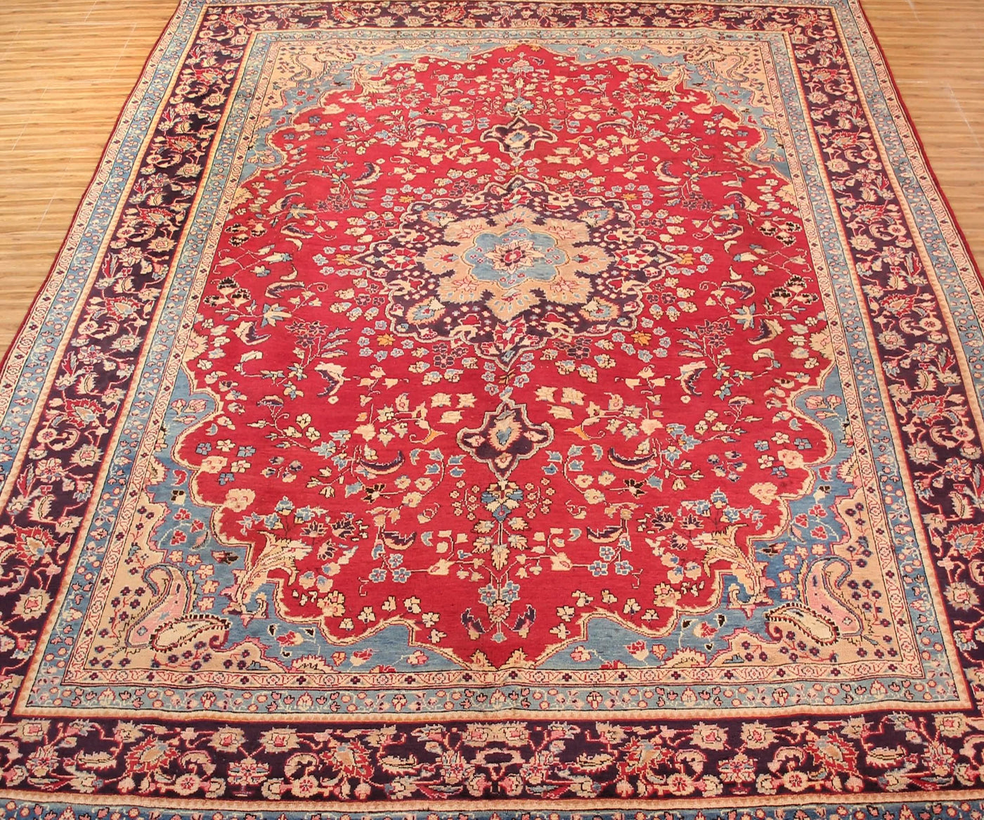 Antique Sabzevar rug featuring elegant central medallion and dense floral vine motifs in red, ivory and blue tones
