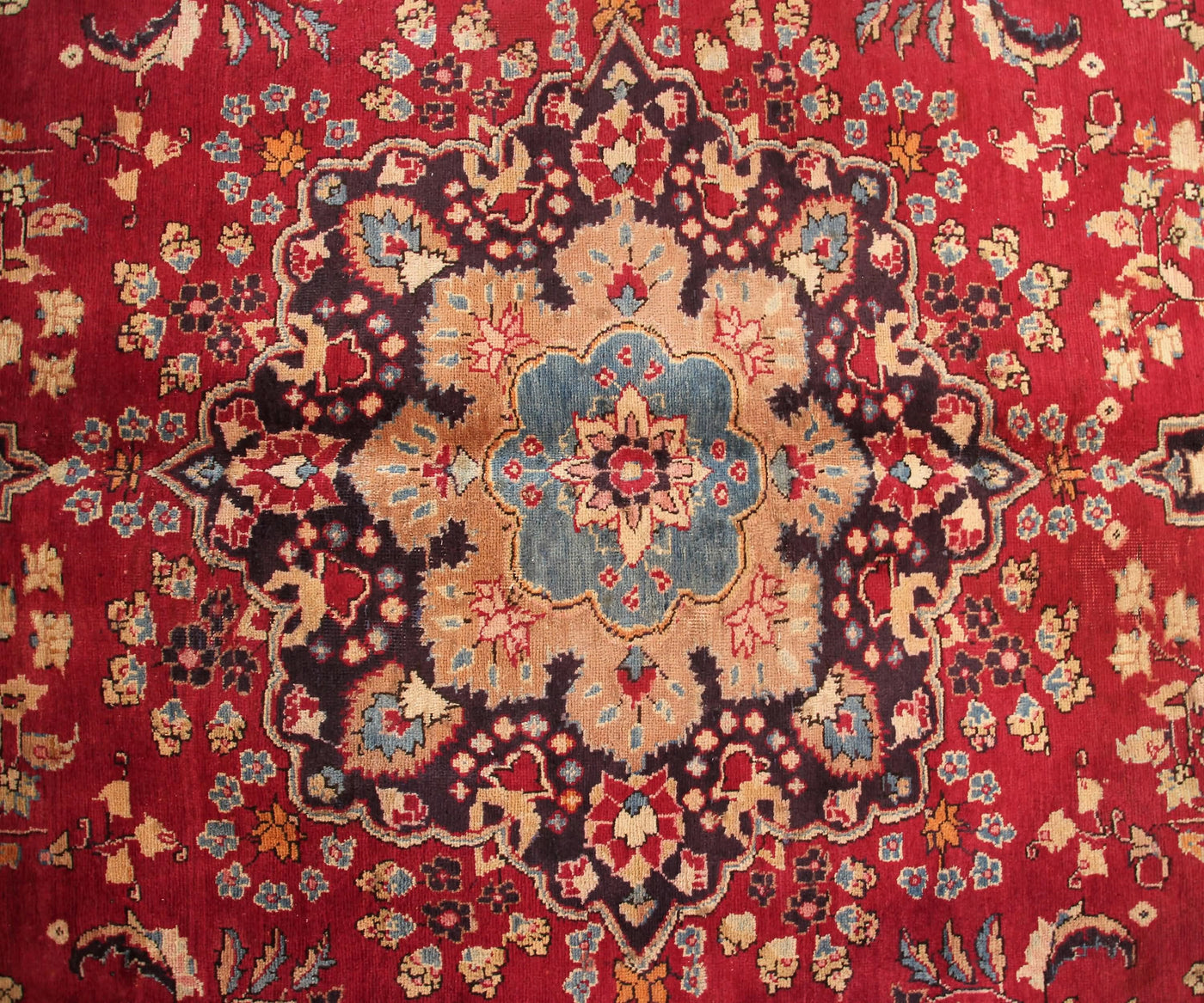 Detailed field view of antique Sabzevar rug highlighting symmetrical floral layout on deep red background
