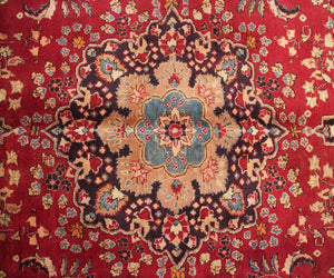 Detailed field view of antique Sabzevar rug highlighting symmetrical floral layout on deep red background
