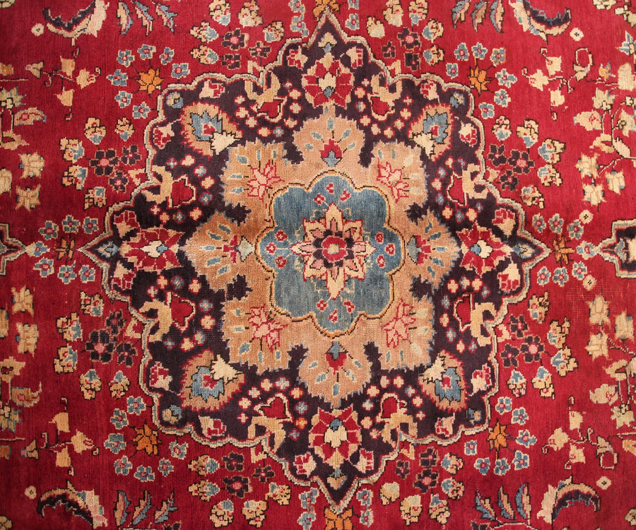 Detailed field view of antique Sabzevar rug highlighting symmetrical floral layout on deep red background
