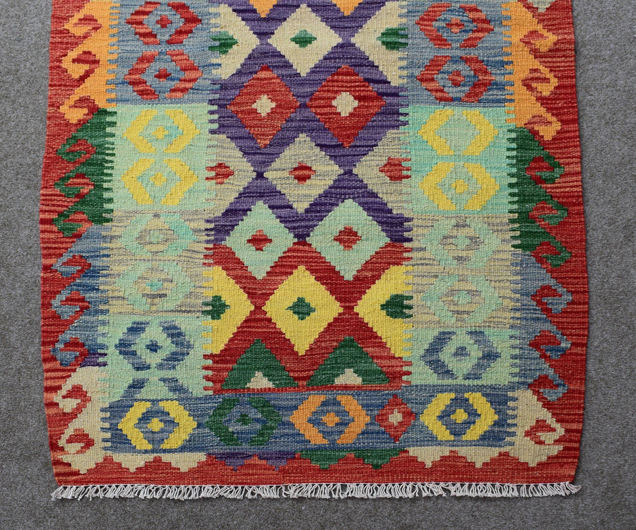 Detailed view of kilim runner central geometric pattern in bright red, turquoise, mustard and green tones
