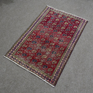 Vintage Persian Shiraz rug 90x134 cm photographed at an angle showing red field with repeating tribal medallions and patterned border