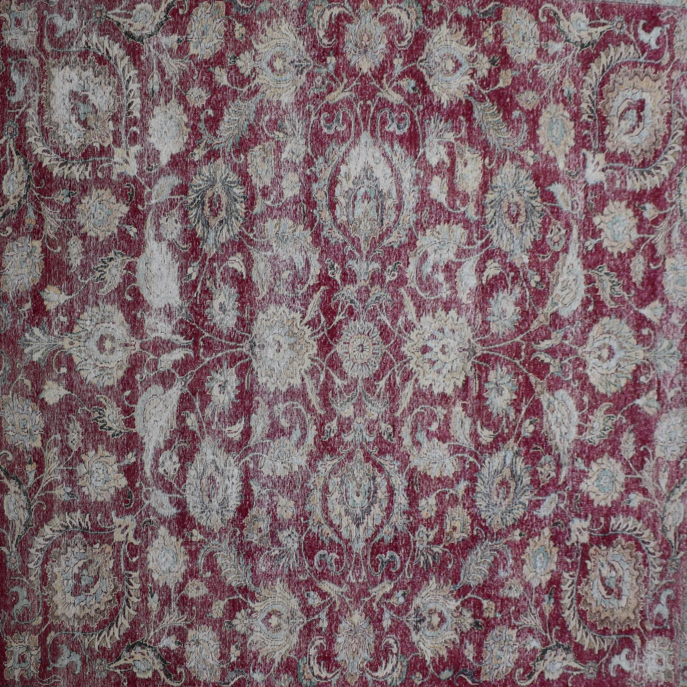 Close up of distressed Persian rug showing worn red background with repeating floral medallion motifs
