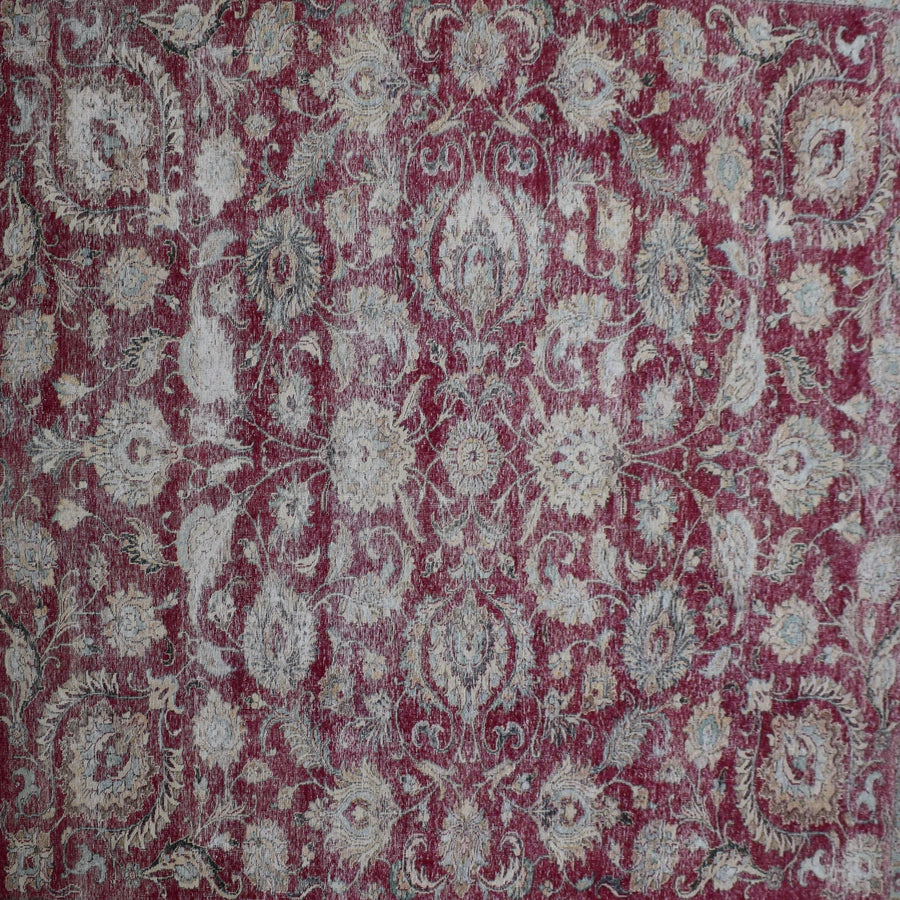 Close up of distressed Persian rug showing worn red background with repeating floral medallion motifs