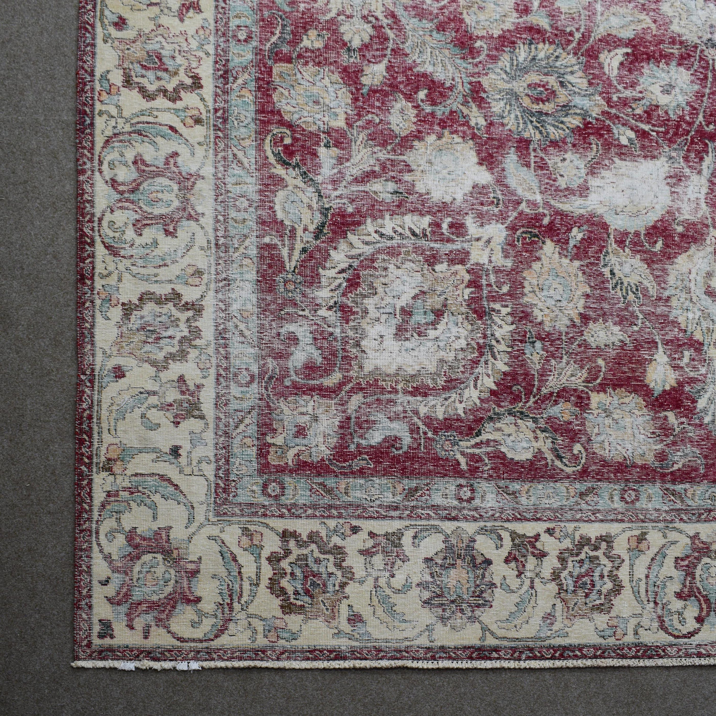 Corner detail of distressed Persian rug with ornate floral border and aged red field pattern