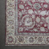 Corner detail of distressed Persian rug with ornate floral border and aged red field pattern