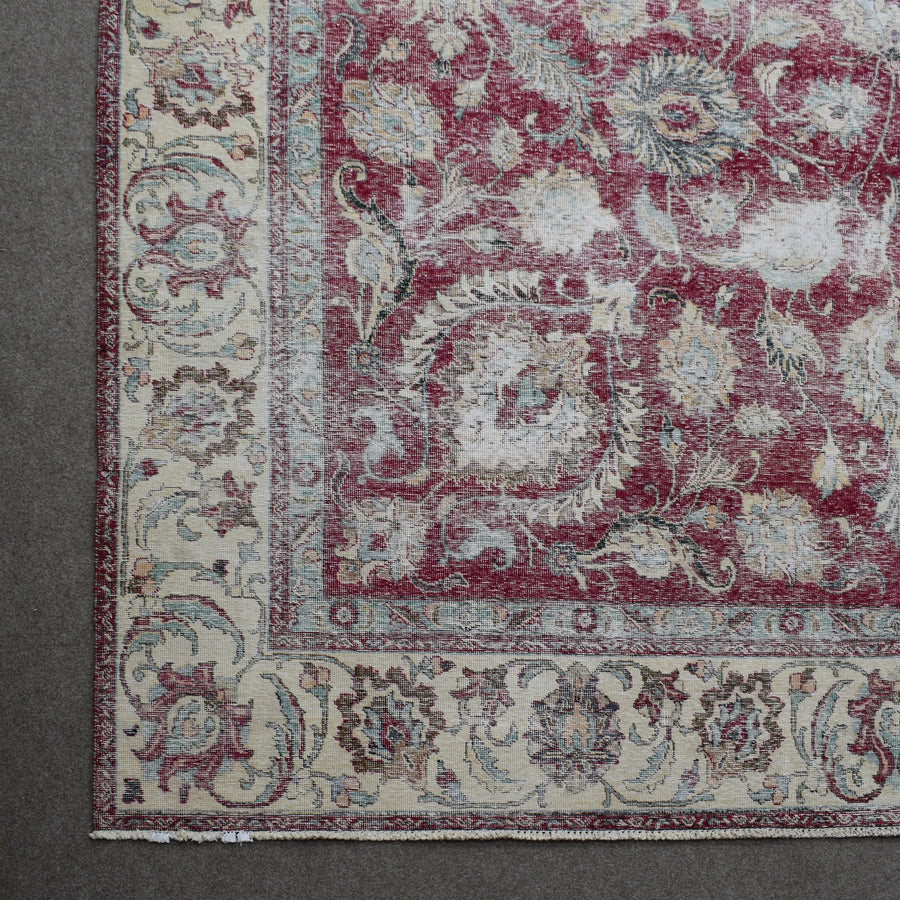 Corner detail of distressed Persian rug with ornate floral border and aged red field pattern