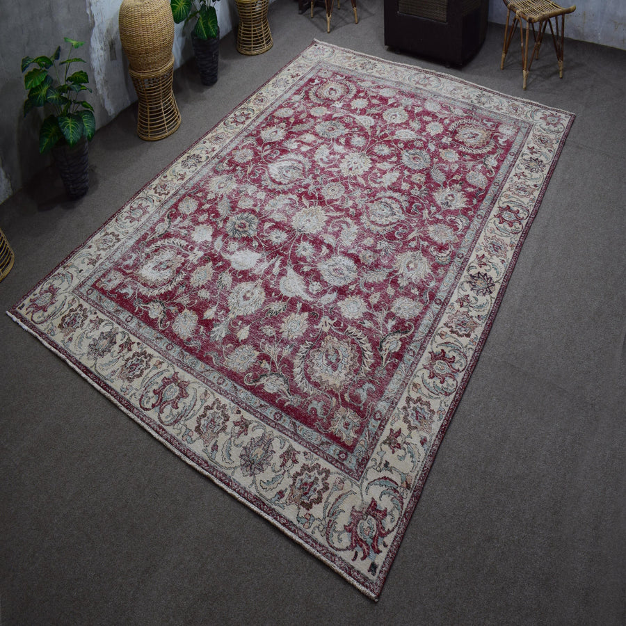 Hand knotted Persian rug photographed at an angle showing large faded floral pattern and decorative border