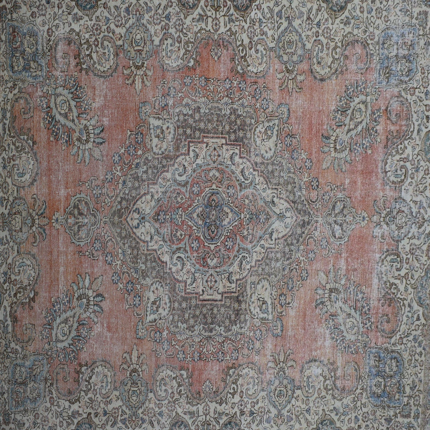 Close up of distressed Persian rug showing central medallion with faded blue and ivory floral motifs