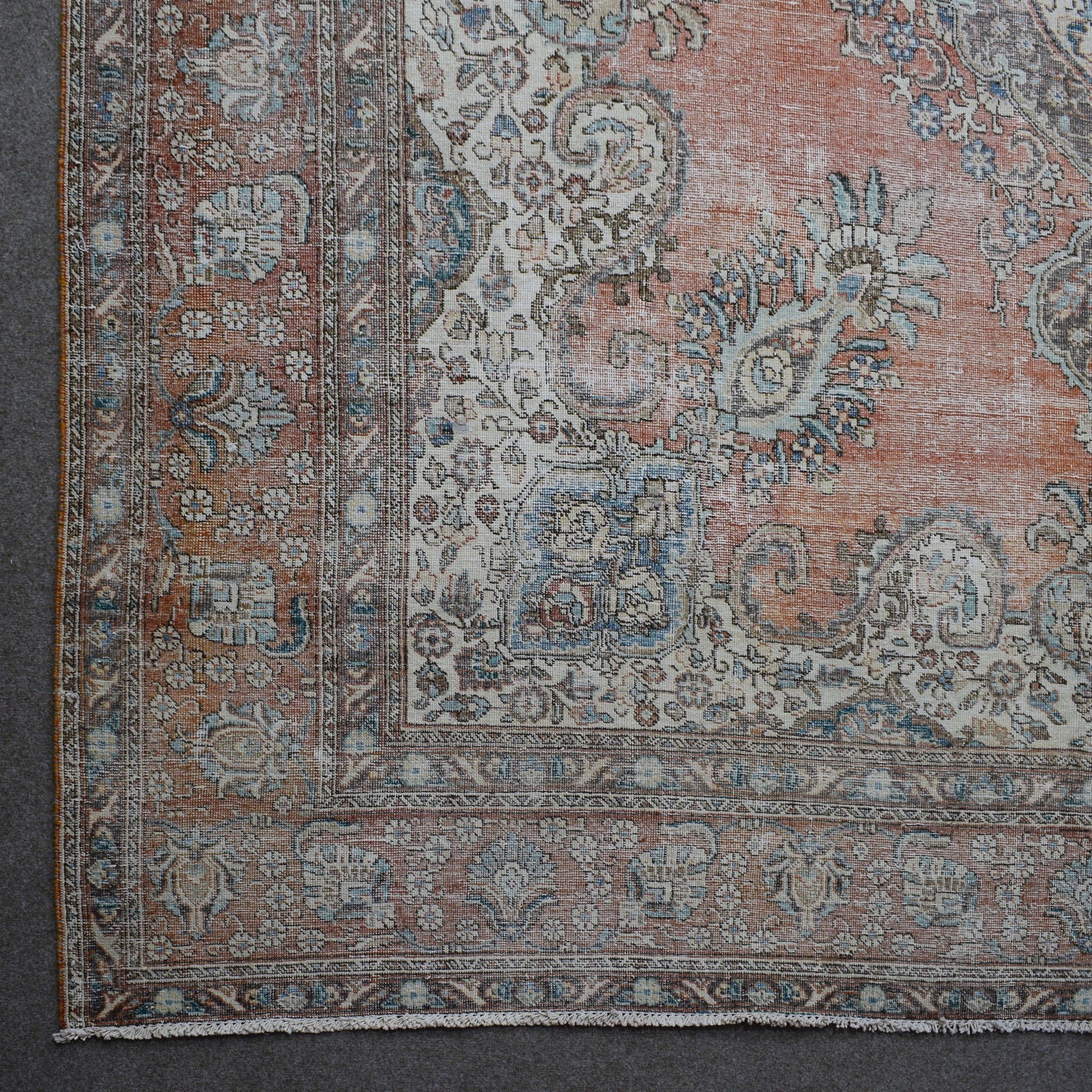 Corner detail of distressed Persian rug with decorative floral border and aged terracotta field