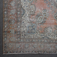Corner detail of distressed Persian rug with decorative floral border and aged terracotta field