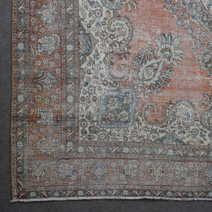 Corner detail of distressed Persian rug with decorative floral border and aged terracotta field