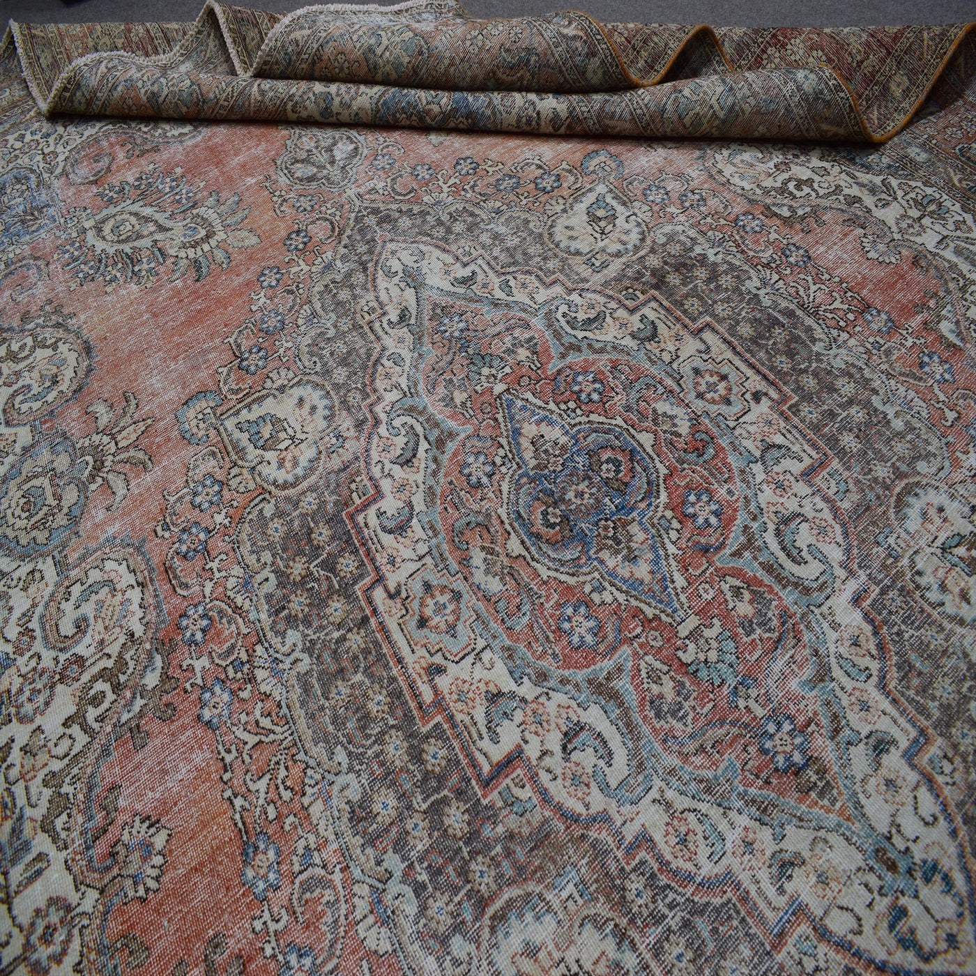 Close up of Persian rug medallion area showing intricate floral patterns in faded terracotta and blue