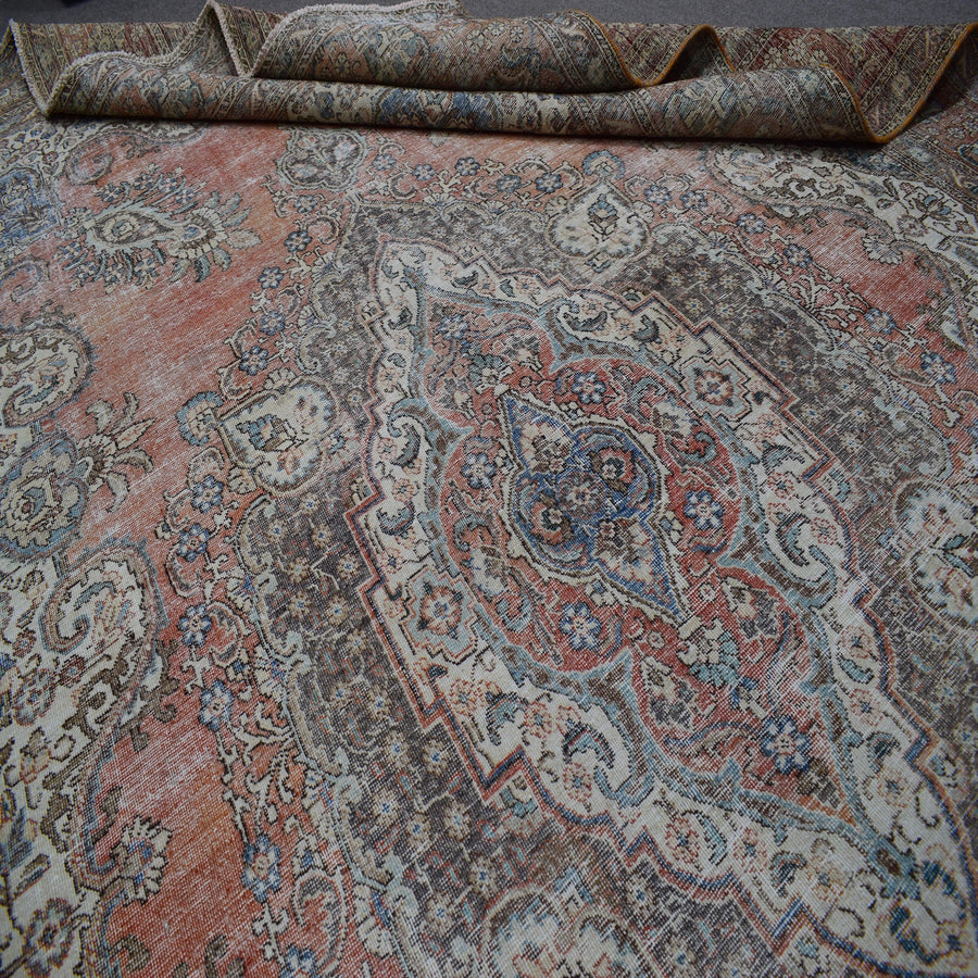 Close up of Persian rug medallion area showing intricate floral patterns in faded terracotta and blue