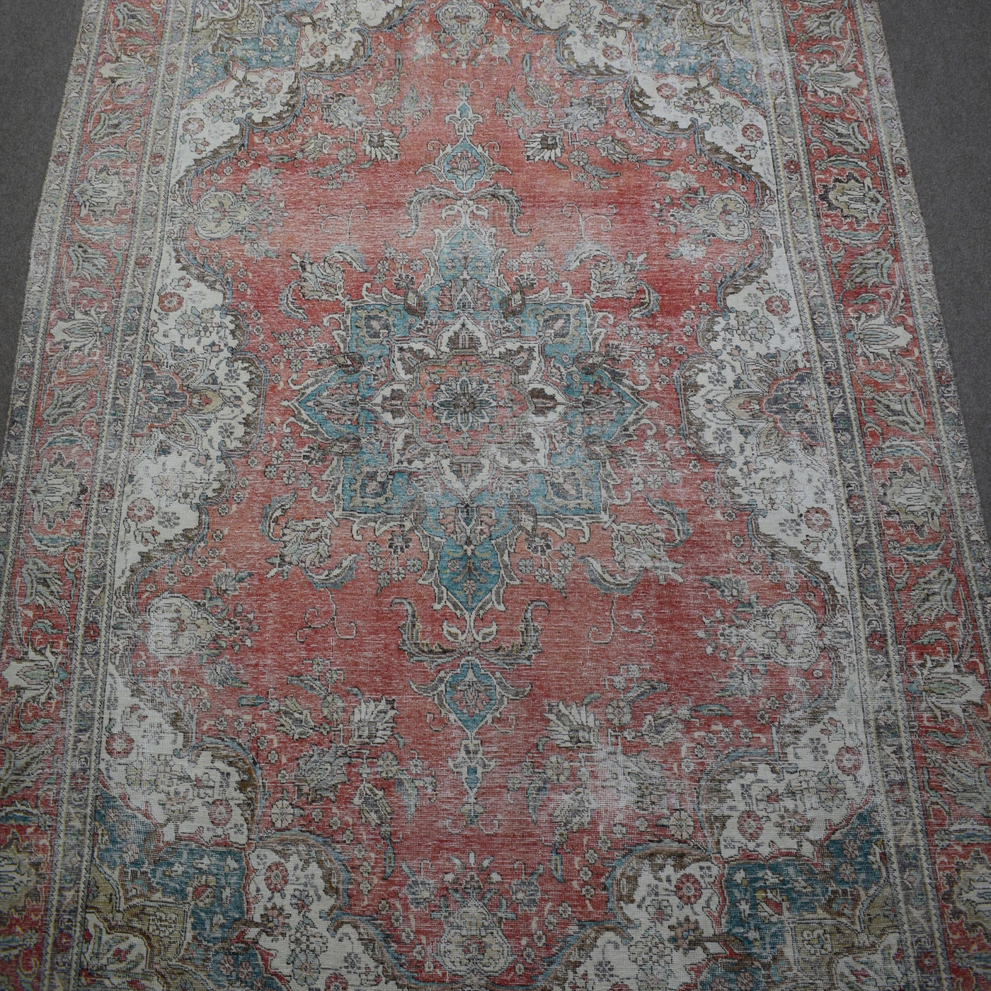 Close up of distressed Persian rug showing central medallion with faded blue and ivory floral motifs