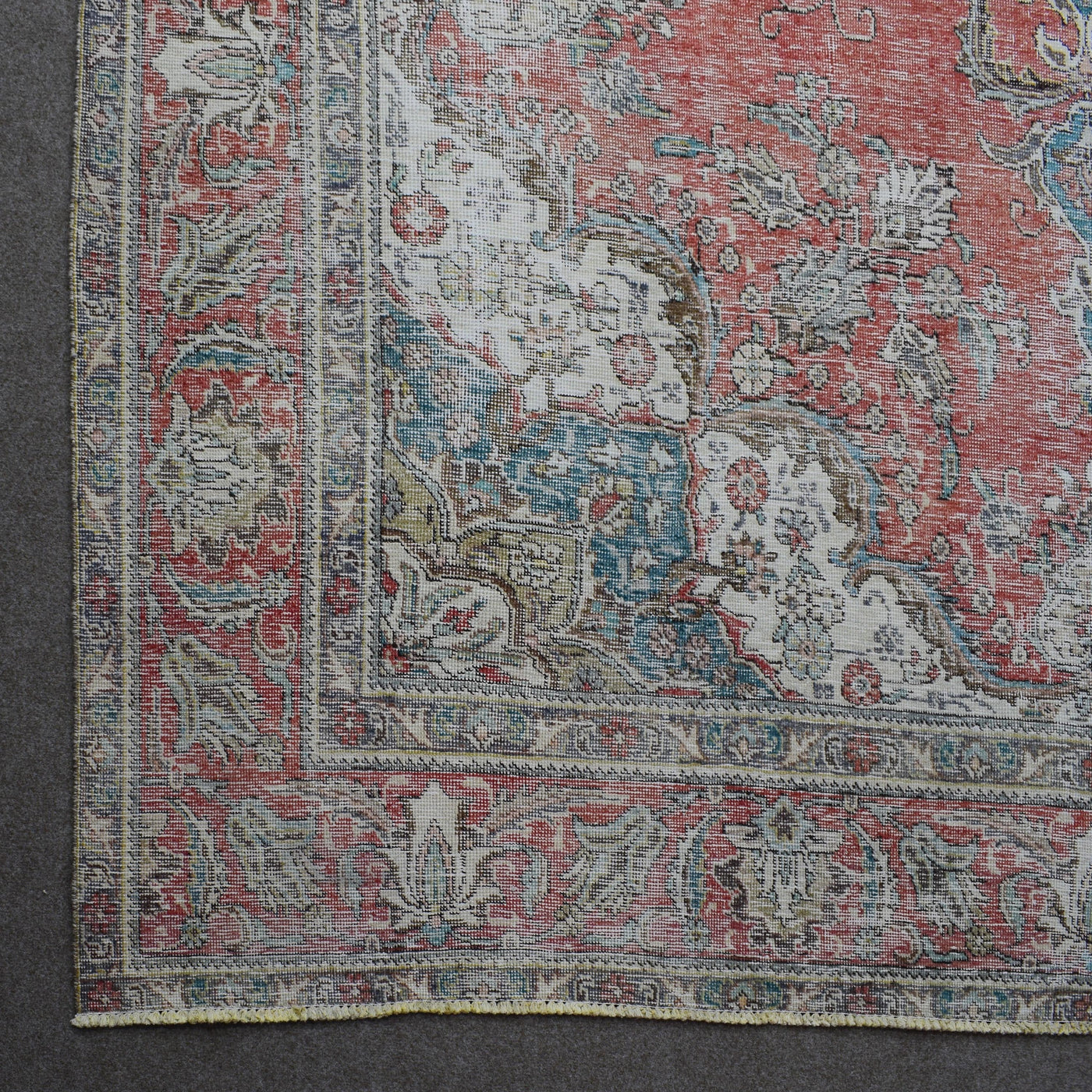 Corner detail of distressed Persian rug with floral border and traditional Persian motifs