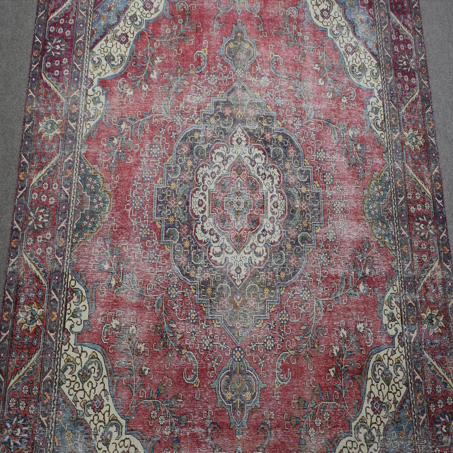 Close up of distressed Persian rug showing faded central medallion with ivory and blue floral motifs