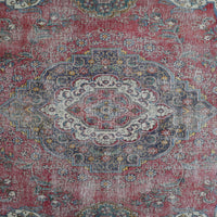 Detailed view of vintage Persian rug medallion featuring intricate floral patterns on a distressed red background