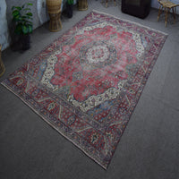 Hand knotted Persian rug photographed at an angle showing overall medallion layout and distressed vintage palette