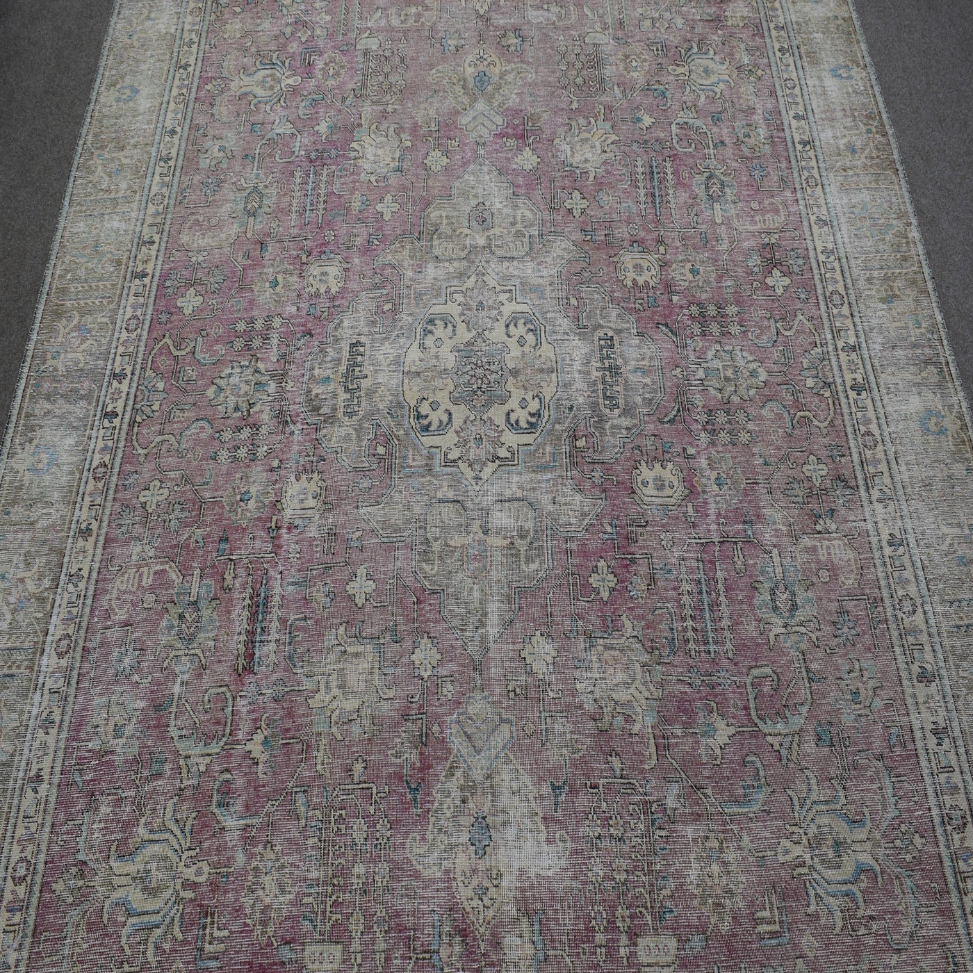 Close up of distressed Persian rug showing worn floral motifs on faded rose background