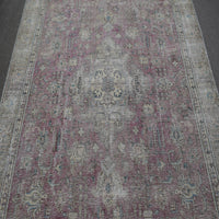 Close up of distressed Persian rug showing worn floral motifs on faded rose background