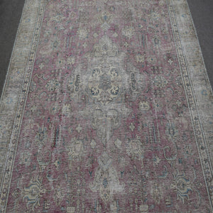 Close up of distressed Persian rug showing worn floral motifs on faded rose background
