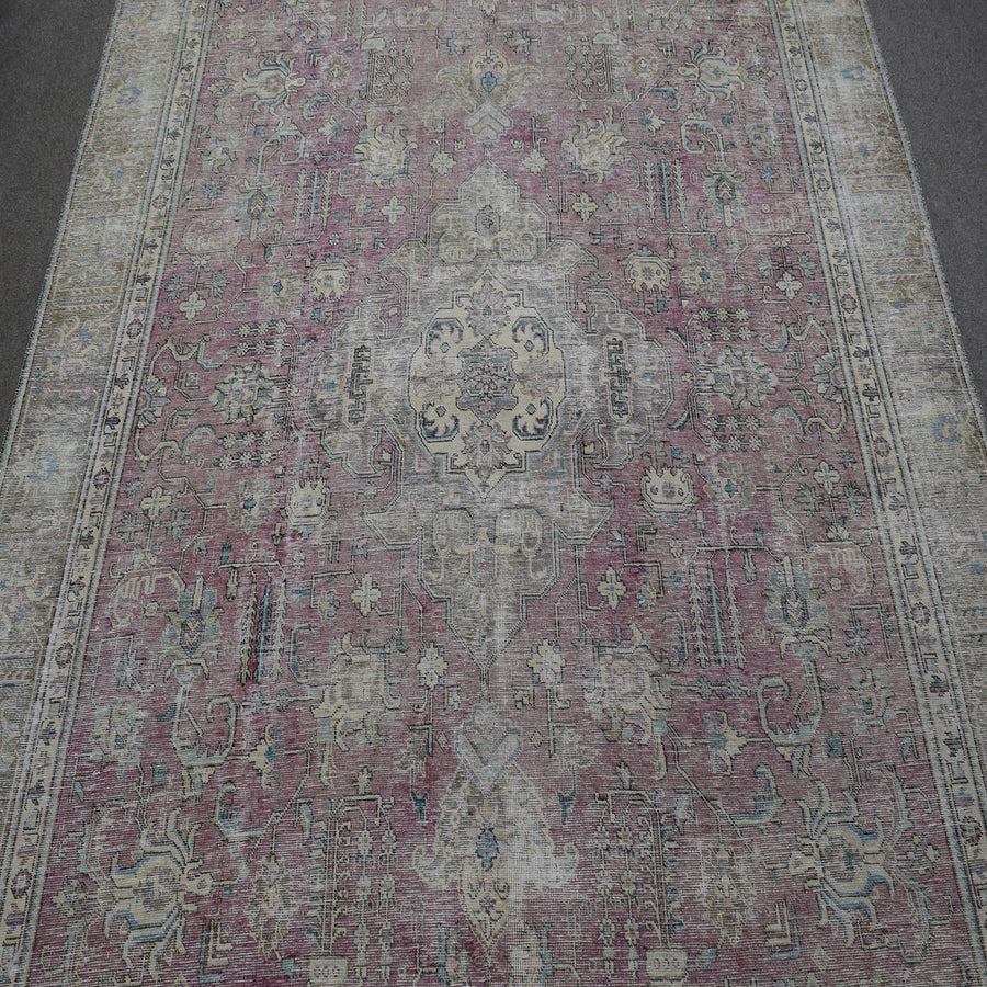 Close up of distressed Persian rug showing worn floral motifs on faded rose background