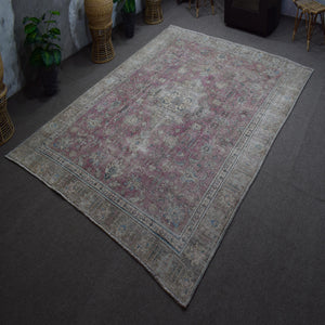 Hand knotted Persian rug photographed at an angle showing overall distressed pattern and muted color palette