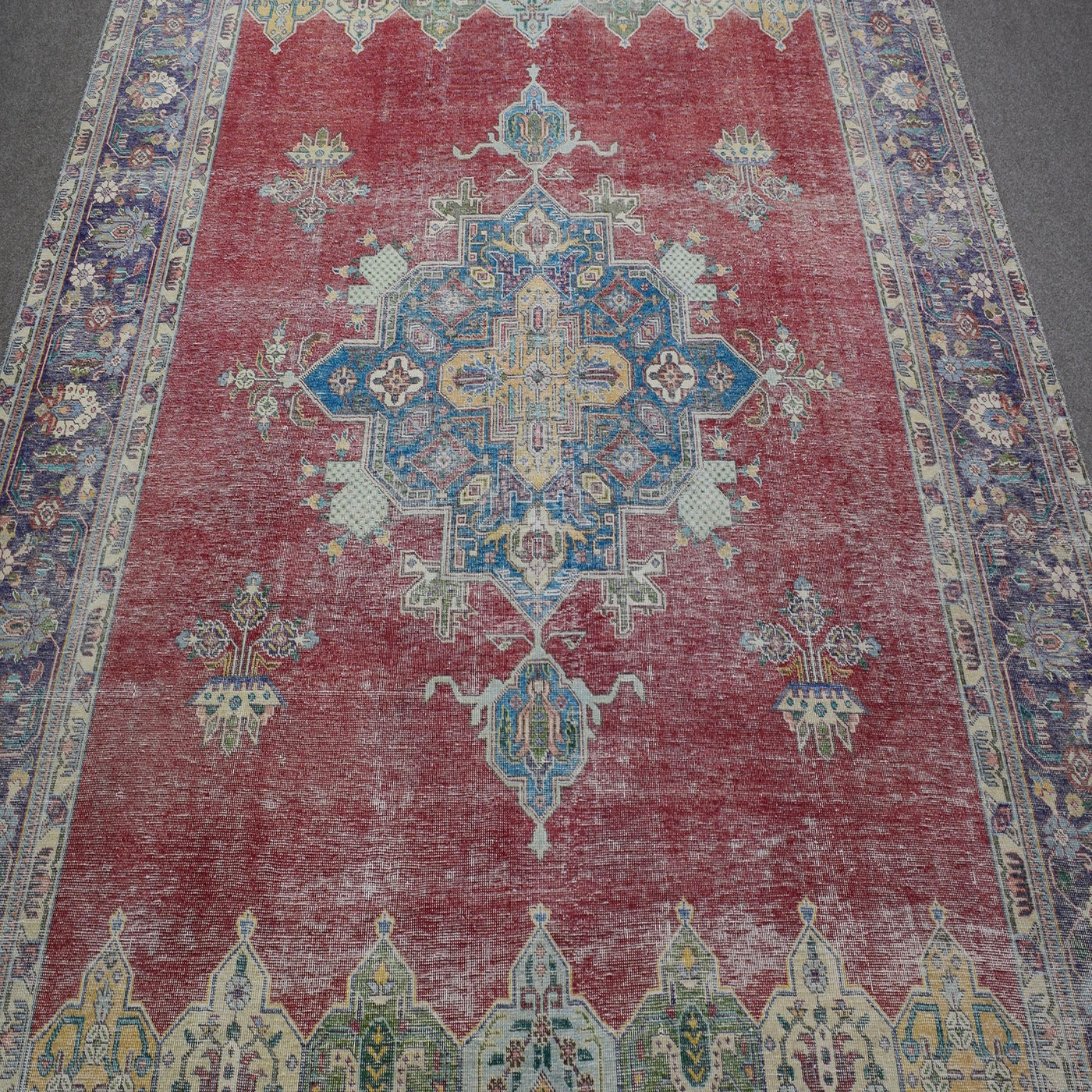 Close up of distressed Persian rug showing geometric medallion with blue and ivory motifs on red field