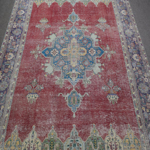 Close up of distressed Persian rug showing geometric medallion with blue and ivory motifs on red field