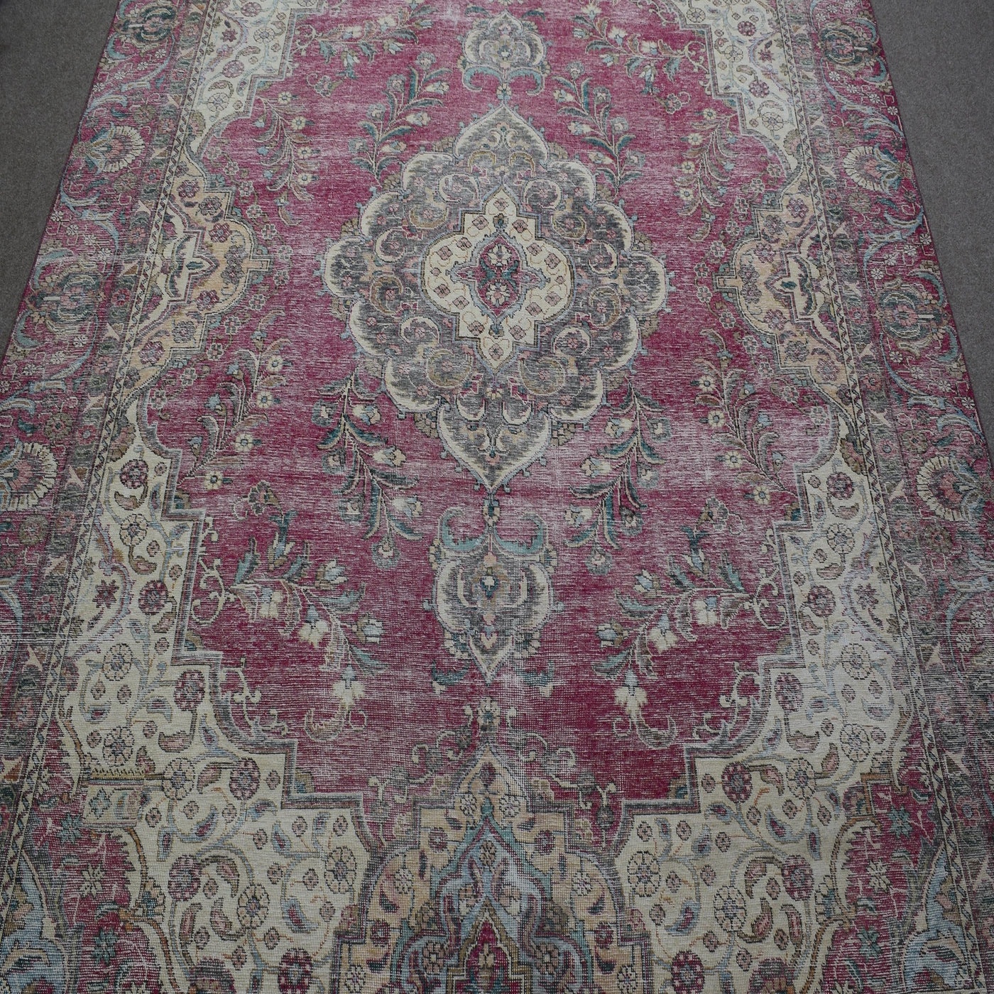 Close up of distressed Persian rug showing intricate floral medallion on faded rose background