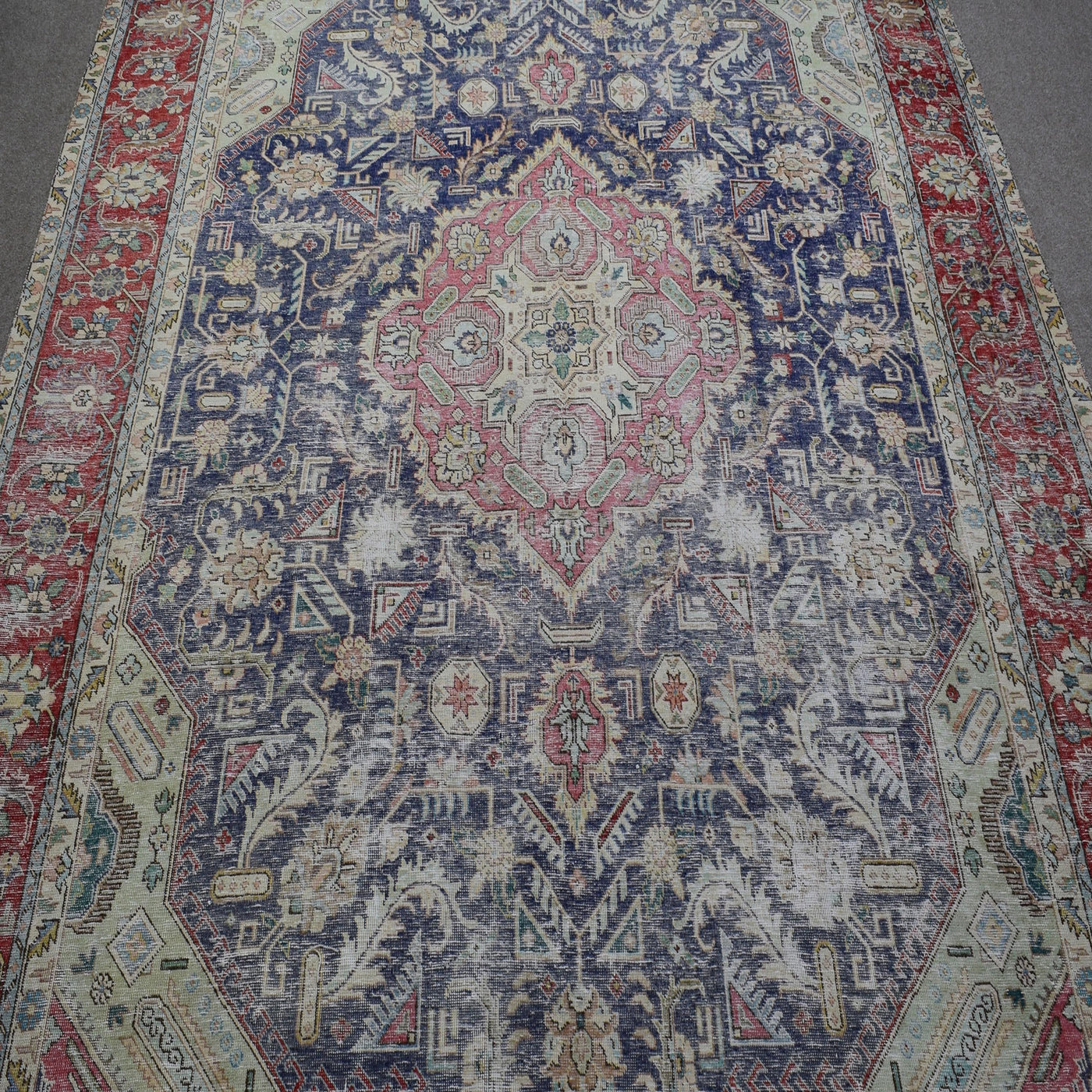 Close up of distressed Persian rug showing intricate floral medallion with pink and ivory motifs on navy field