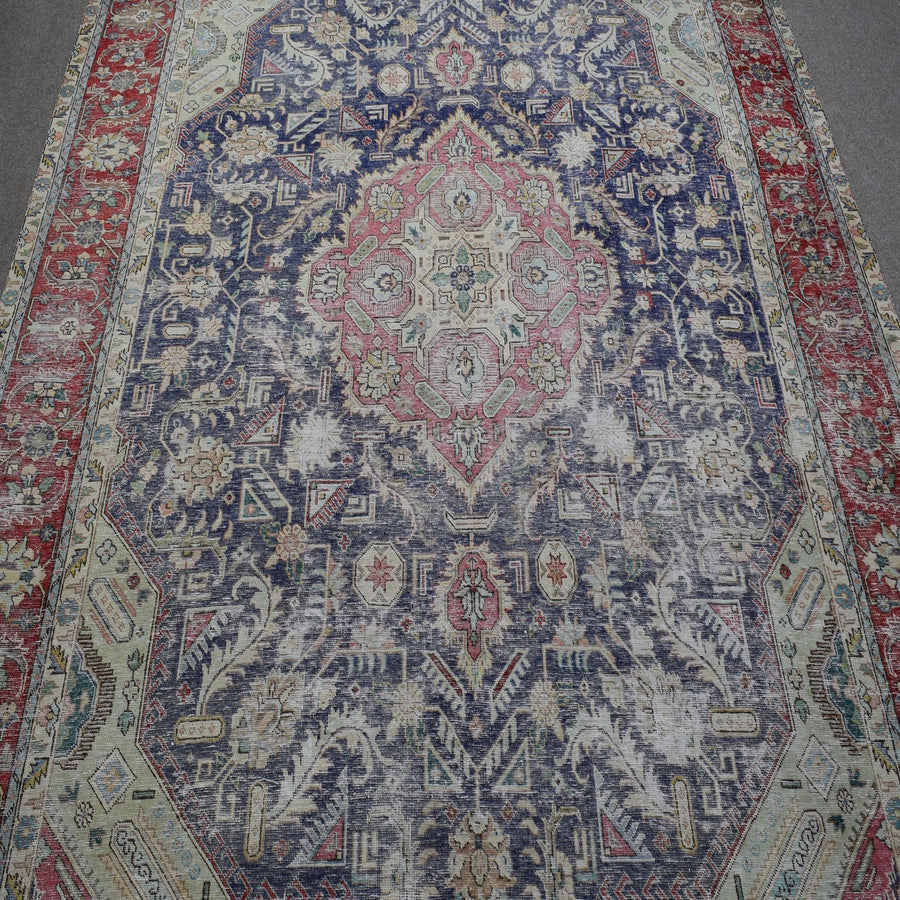 Close up of distressed Persian rug showing intricate floral medallion with pink and ivory motifs on navy field