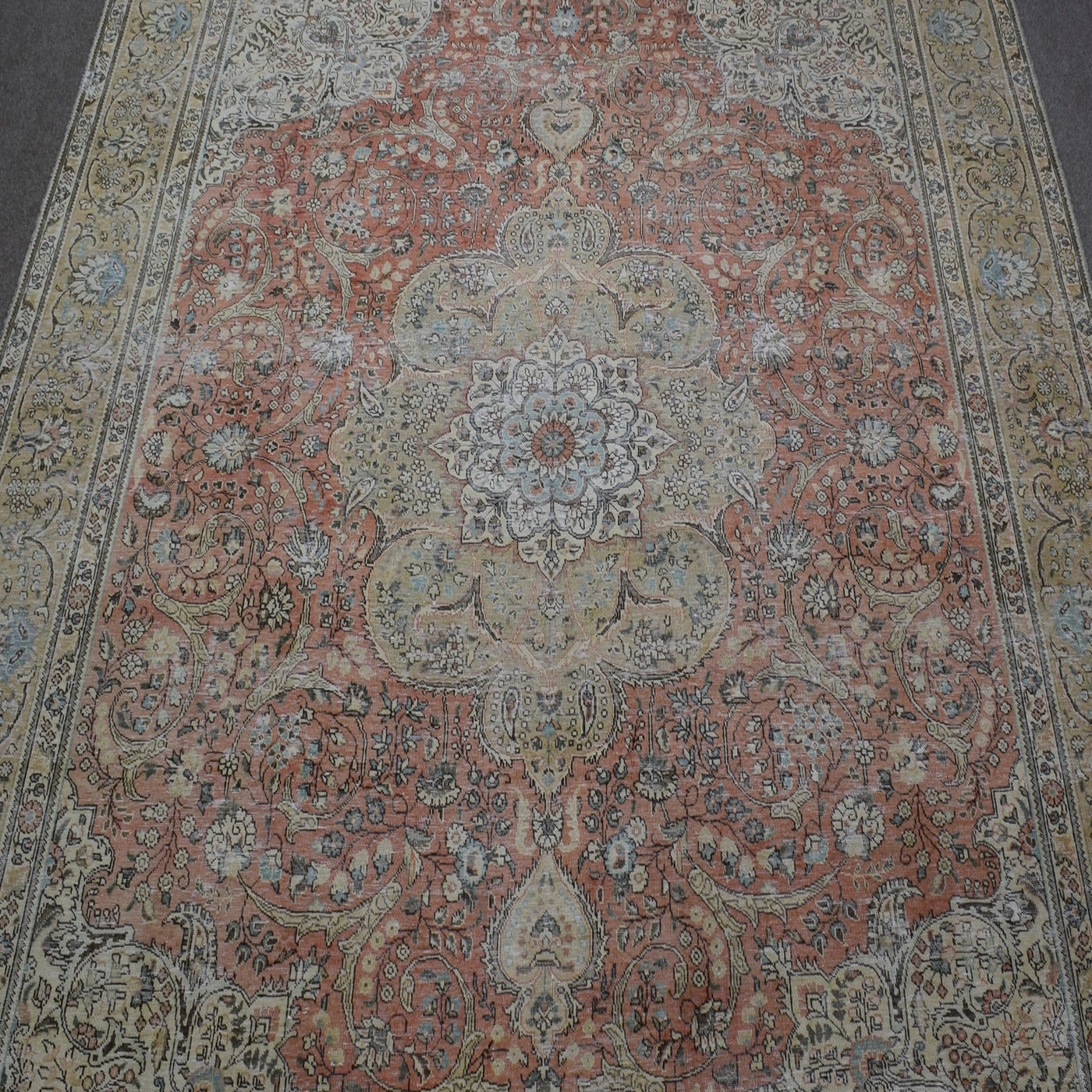 Close up of distressed Persian rug showing intricate floral medallion on faded coral background