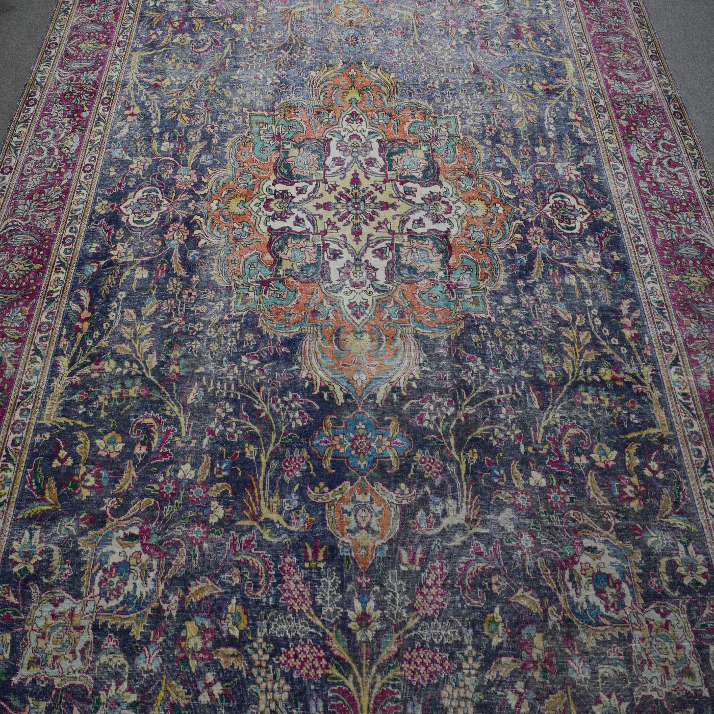 Close up of distressed Persian rug showing detailed floral medallion with ivory and orange accents