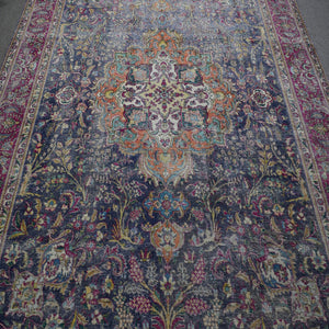 Close up of distressed Persian rug showing detailed floral medallion with ivory and orange accents