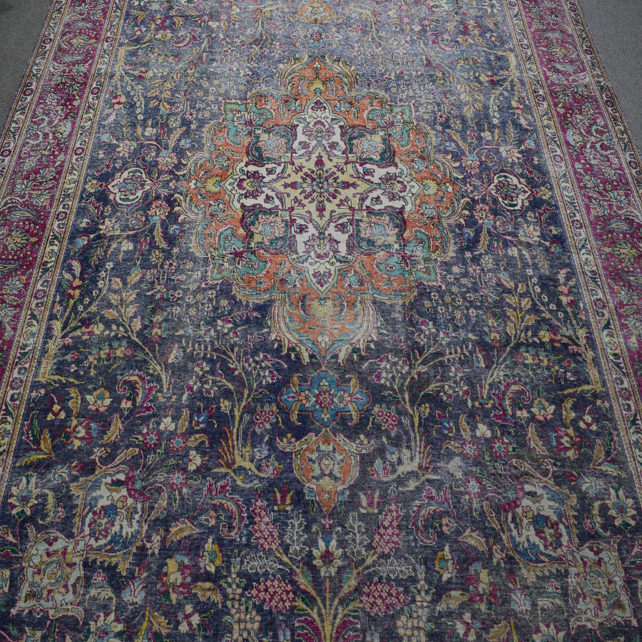 Close up of distressed Persian rug showing detailed floral medallion with ivory and orange accents
