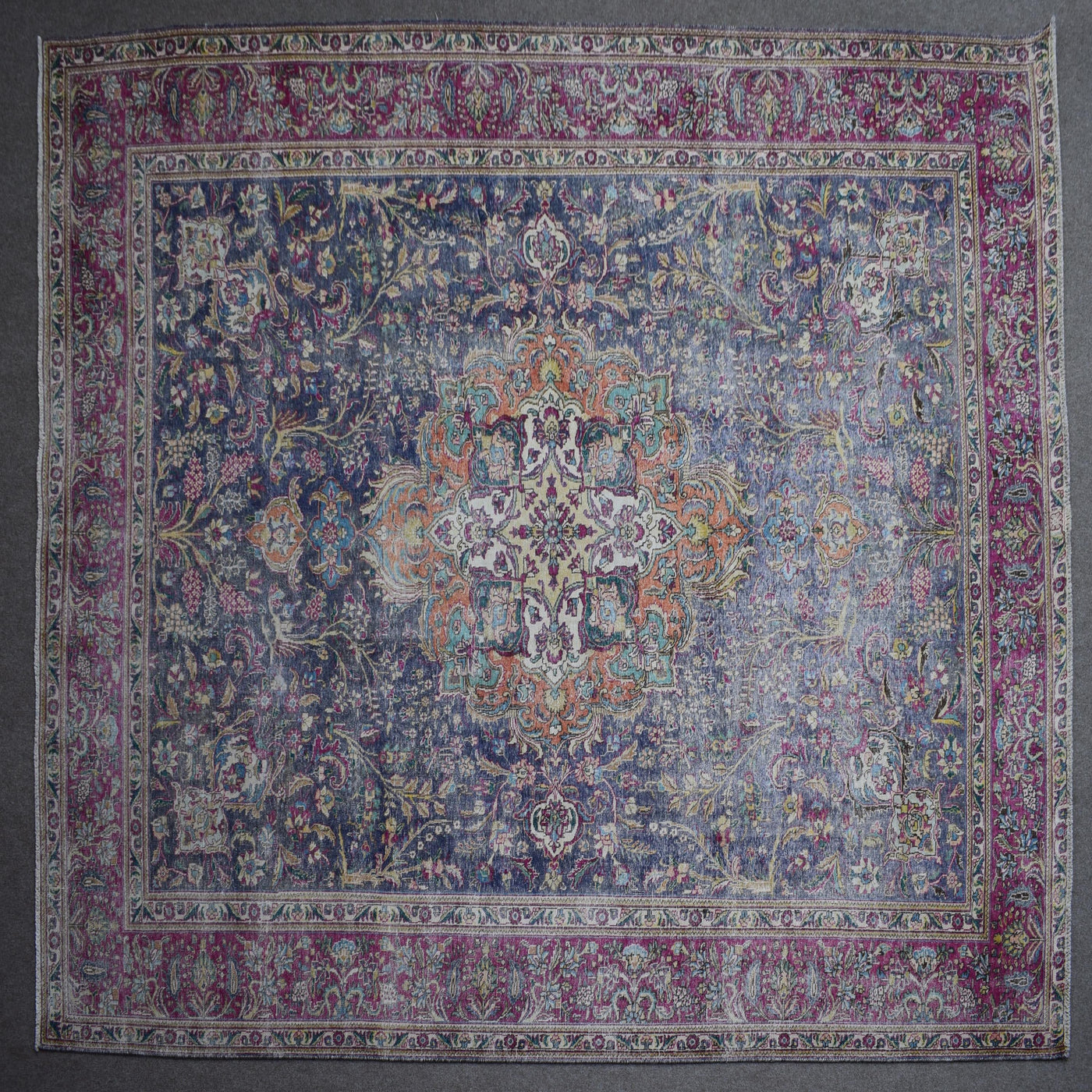 Hand knotted Persian rug photographed at an angle showing overall medallion layout and distressed navy tones