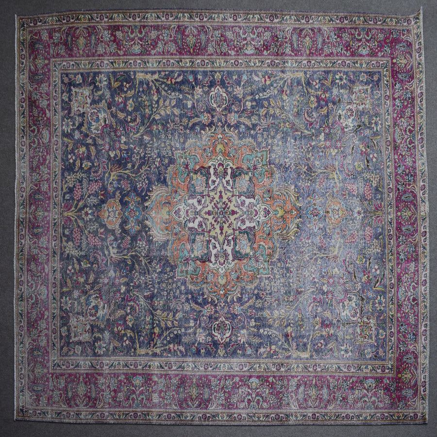 Hand knotted Persian rug photographed at an angle showing overall medallion layout and distressed navy tones