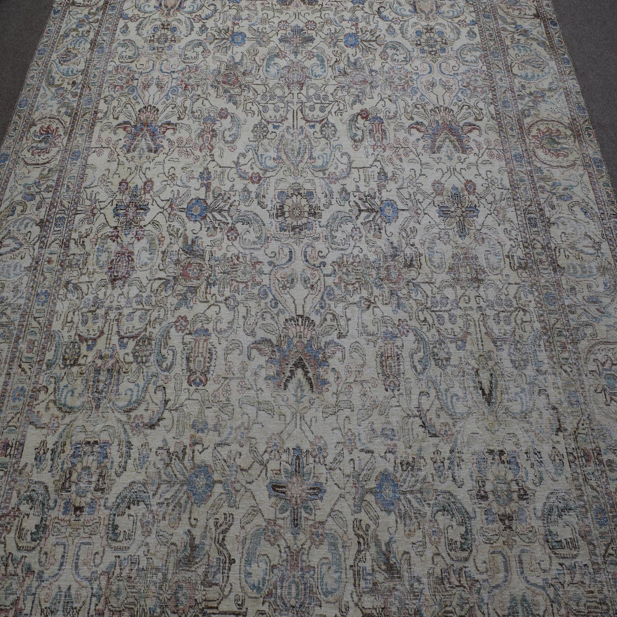 Close up of distressed Persian rug showing intricate floral motifs on faded ivory background