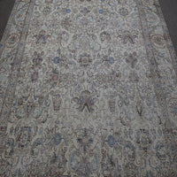 Close up of distressed Persian rug showing intricate floral motifs on faded ivory background