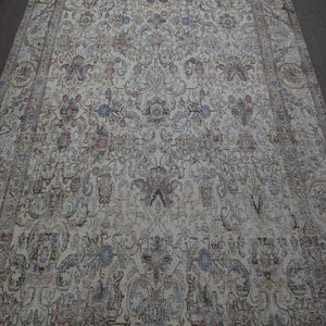 Close up of distressed Persian rug showing intricate floral motifs on faded ivory background