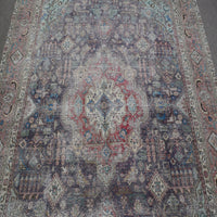 Close up of distressed Persian rug showing intricate medallion with red and ivory floral motifs