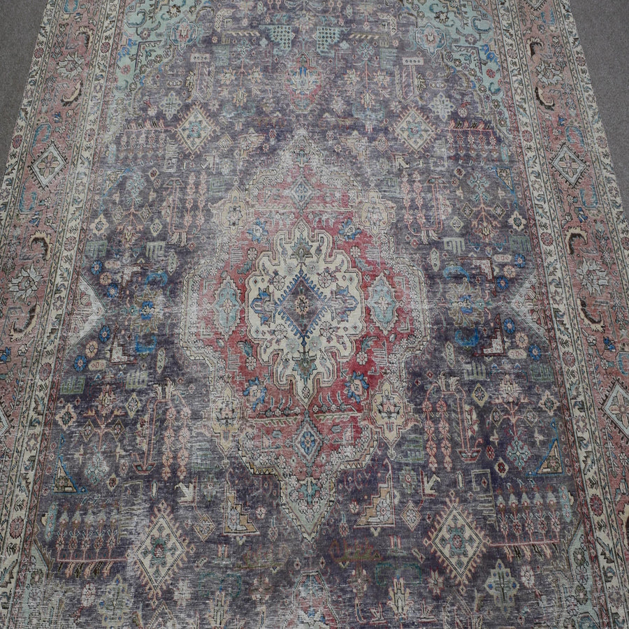 Close up of distressed Persian rug showing intricate medallion with red and ivory floral motifs