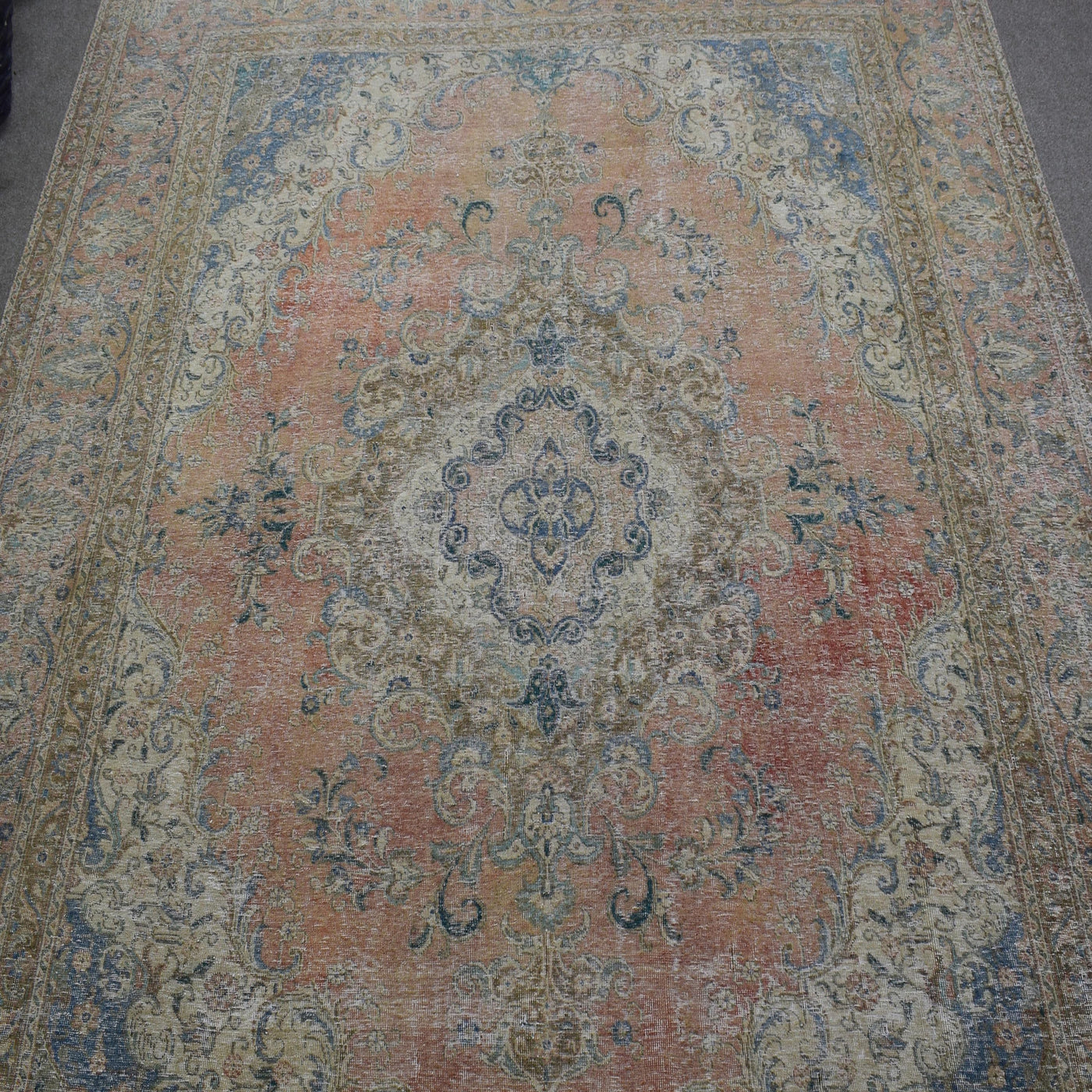Close up of distressed Persian rug showing ornate central medallion with blue and ivory floral motifs
