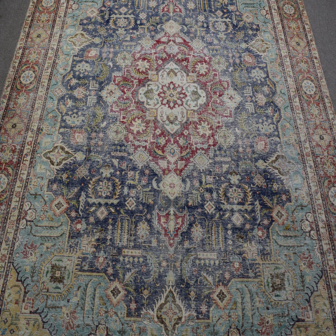 Close up of distressed Persian rug showing intricate floral medallion with red and ivory motifs